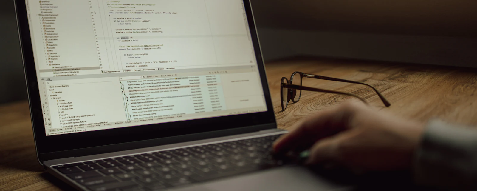 Hands on a laptop showing source code, reading glasses beside it